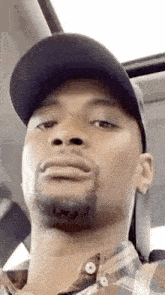 a man wearing a hat and plaid shirt is making a funny face while sitting in a car .