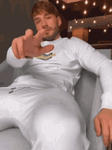 a man with a beard wearing a white shirt and white pants is pointing at the camera