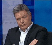 a man in a suit and white shirt with his arms crossed looks at the camera