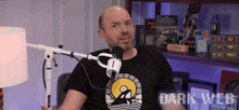 a man sitting in front of a microphone wearing a dark web t shirt