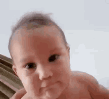 a baby without a shirt is looking at the camera .