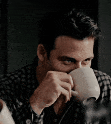 a man in a plaid shirt is drinking from a white cup