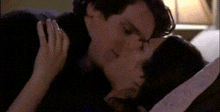 a man and a woman are kissing on a couch while the man is reading a book .