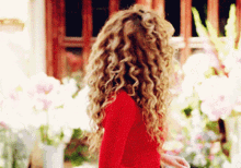 a woman with long curly hair is wearing a red top