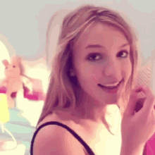 a woman in a black tank top is smiling and holding a comb in her hand