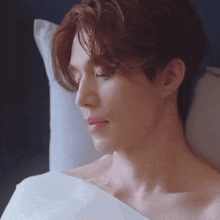 a shirtless man is laying in a bed with his eyes closed and a pillow .
