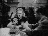 a black and white photo of a man and woman sitting at a table holding hands