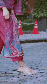 a woman wearing a pink dress and white heels is walking down a sidewalk .