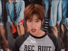 a young man wearing a shirt that says rec butt is standing in front of a group of men in school uniforms .