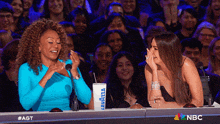 two women are sitting at a table with a cup that says lavazza on it