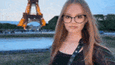 a woman wearing glasses stands in front of the eiffel tower in paris