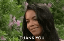 a woman is smiling and saying `` thank you '' while standing in front of flowers .