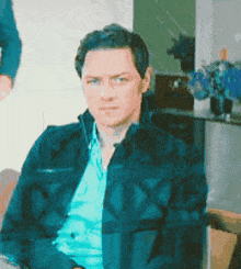 a man in a blue shirt and a black jacket is sitting on a couch .