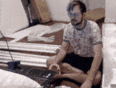 a man in a floral shirt sits on the floor with a laptop and a box that says ' ikea ' on it