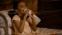 a little girl is drinking from a cup while laying on a bed with a string around her mouth