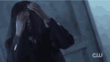 a woman in a black jacket is covering her face with her hands .
