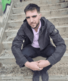 a man in a black jacket sits on a set of concrete steps