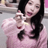 a woman in a pink sweater is holding a spoon in her hand