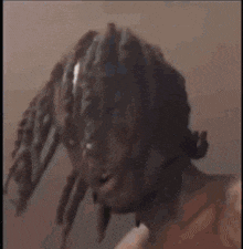 a man with dreadlocks is standing in front of a wall and looking at the camera .