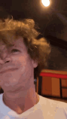a man with curly hair is wearing a white shirt and gold chain around his neck