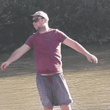 a man wearing a hat and sunglasses stands in the water with his arms outstretched