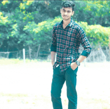 a young man wearing a plaid shirt and a watch stands in a field