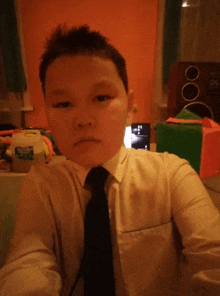 a young man in a white shirt and black tie is taking a selfie with a bottle of aquafina water behind him