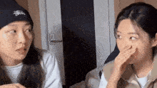 two young women are sitting next to each other and one of them is wearing a hat that says stussy on it .