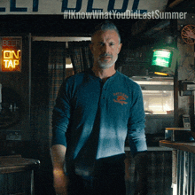 a man in a blue shirt is standing in front of a sign that says beer on tap
