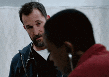 a man with a beard and a stethoscope around his neck talks to another man