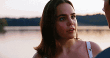 a close up of a woman looking at a man in front of a lake .
