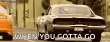 a muscle car is driving down a street next to another car with the words `` when you gotta go '' written on it .