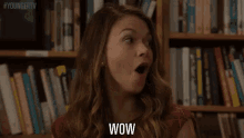 a woman is standing in front of a bookshelf and smiling while saying wow .