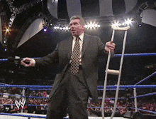a man in a suit and tie is holding crutches in a wrestling ring with the letter w on the ring