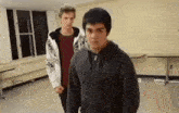 two young men are standing next to each other in a room and one of them is wearing a hoodie .
