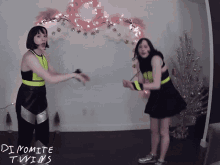 two women are dancing in front of a wall that says dynamite twins on it