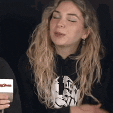 a woman with blonde hair is wearing a black hoodie and earrings .