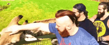 a man with a beard is petting a giraffe while another man looks on .