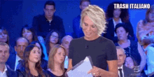 a woman is standing in front of a crowd holding a piece of paper and a sign that says trash italiano .