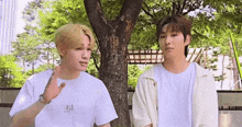 two young men are standing next to each other under a tree .