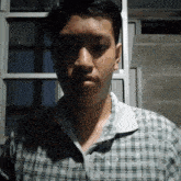 a young man wearing a plaid shirt looks at the camera