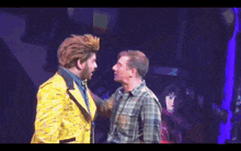 a man in a yellow suit is standing next to another man in a plaid shirt