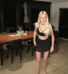 a woman in a black top and skirt stands in front of a table