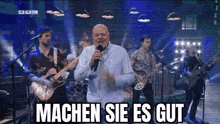 a man is singing into a microphone in front of a group of men playing guitars and drums .