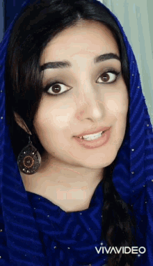 a woman wearing a blue scarf and earrings looks at the camera with vivavideo in the corner