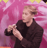 a man in a black jacket is eating an ice cream cone in front of a pink background