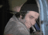 a man wearing a black hat is smiling while looking out a car window