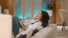 a woman sits on a couch with her eyes closed while using a tablet