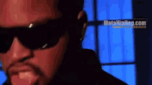 a man wearing sunglasses is standing in front of a window in a dark room .