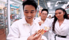 a man in a white jacket is holding a sandwich in his hand while a woman looks on .